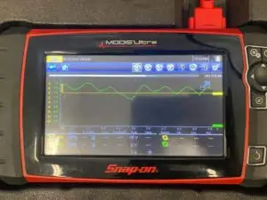 Image of an automotive technician using an oscilloscope to perform a test on a car engine. The oscilloscope is an essential tool for diagnosing problems in the vehicle's electrical system and determining the cause of engine performance failures.