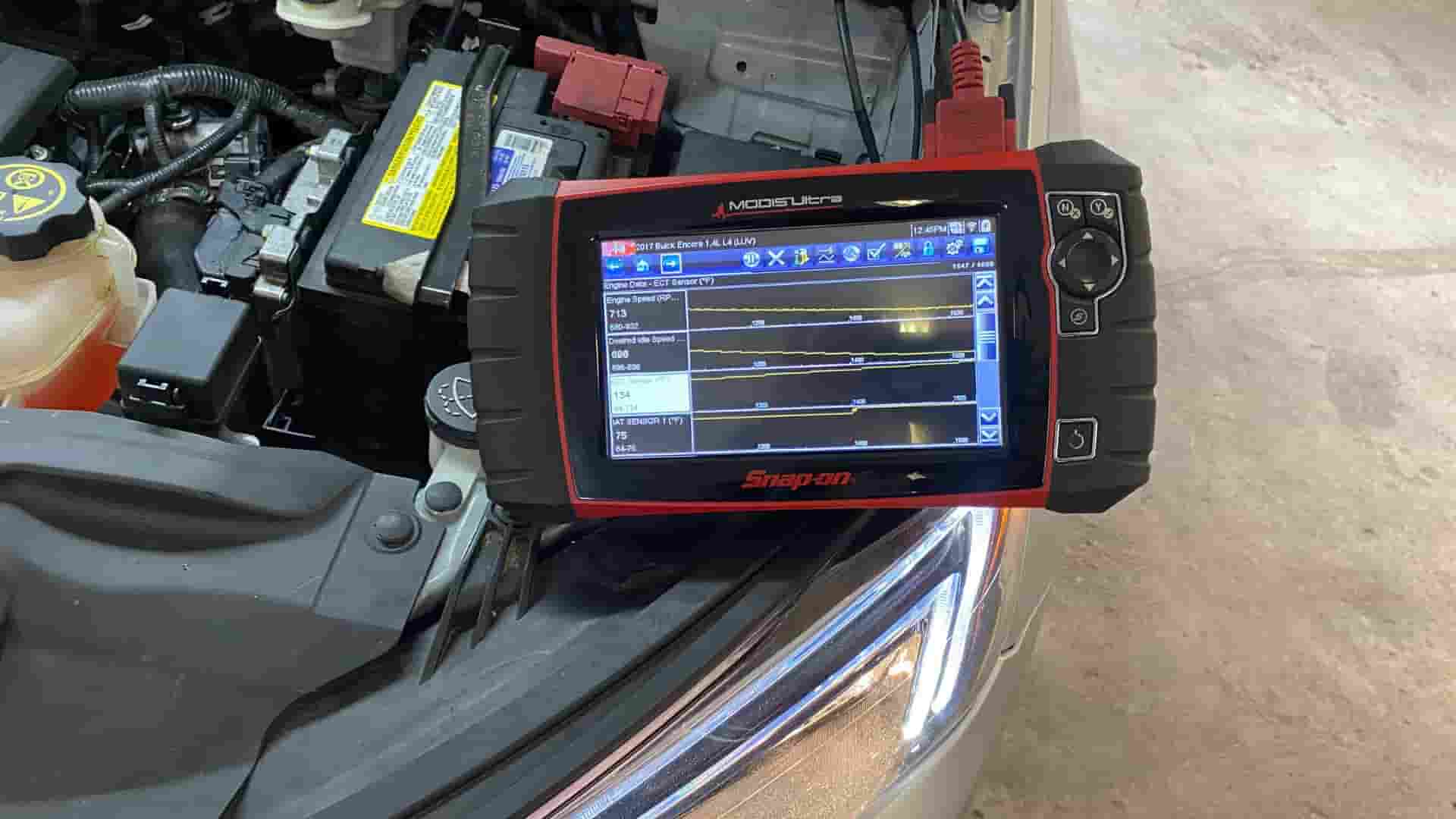 A group of mechanics working on a car engine, with one mechanic using a laptop to re-flash the software on the vehicle's electronic control unit (ECU).