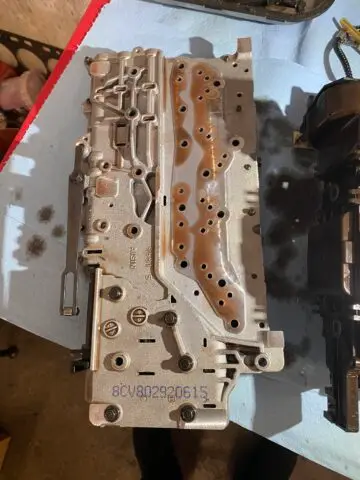 The image shows a valve body from a 6L80 automatic transmission in close-up. The valve body is a rectangular piece of die-cast aluminum with various openings and ports to allow transmission fluid to flow through it. Various valves and solenoids can be seen on top of the valve body, each with a label indicating its function. Some of the labels read "1-2-3-4 clutch solenoid," "2-6 clutch solenoid," and "pressure control solenoid," indicating that these valves and solenoids help control clutch and transmission fluid pressure. the broadcast. In general, the image shows the complexity and precision of the design of the valve bodies of modern automatic transmissions.